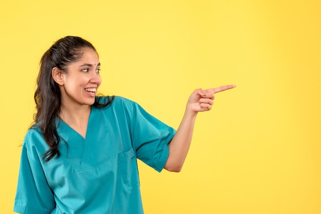 Vista frontal feliz doctora en uniforme de pie sobre fondo amarillo aislado