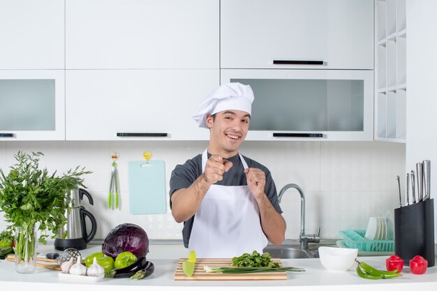 Vista frontal feliz joven chef en uniforme apuntando a la cámara