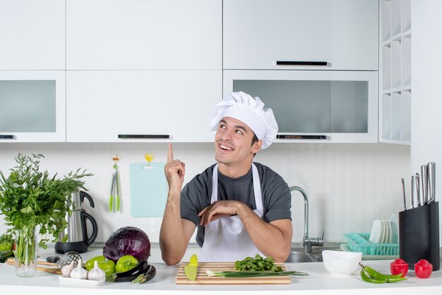 Vista frontal feliz joven cocinero en uniforme apuntando al armario de la cocina