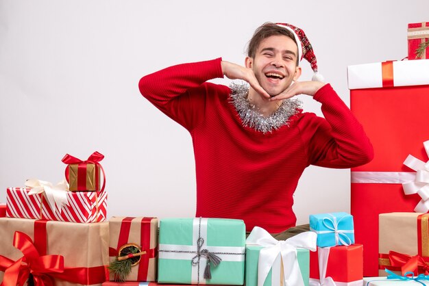 Vista frontal feliz joven con máscara sentado alrededor de regalos de Navidad