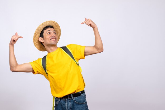 Vista frontal feliz joven con sombrero de paja y camiseta amarilla apuntando a sí mismo