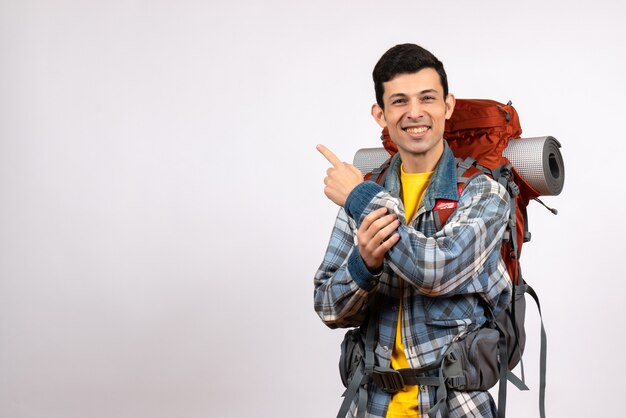 Vista frontal feliz joven viajero con mochila apuntando hacia atrás