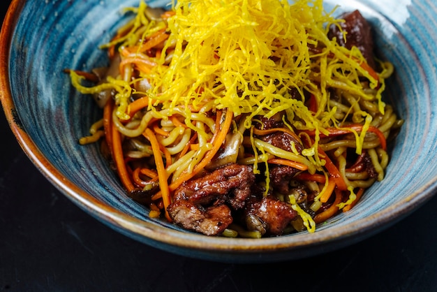 Vista frontal de fideos con verduras fritas y carne con queso rallado en un tazón