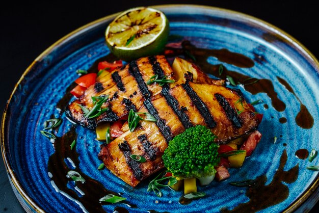 Vista frontal filete de pescado a la parrilla con verduras y una rodaja de limón en un plato