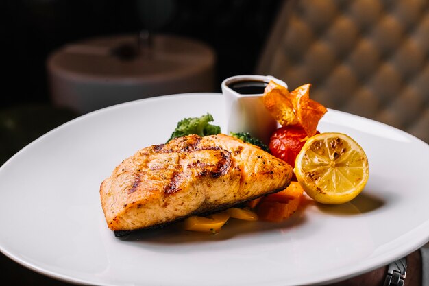 Vista frontal filete de pescado rojo a la parrilla con brócoli, una rodaja de tomate limón y salsa de narsharab