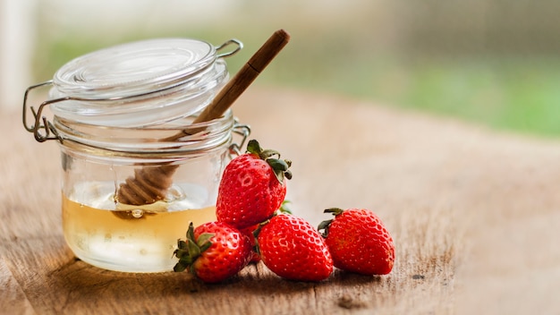 Foto gratuita vista frontal de fresas cerca de tarro de miel