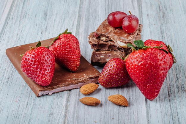 Vista frontal de fresas con chocolate y almendras sobre una superficie gris