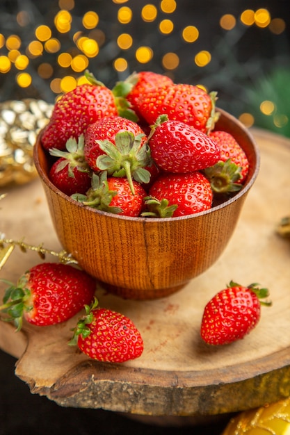 Vista frontal de fresas frescas alrededor de juguetes navideños en el fondo oscuro sabor a fruta foto navideña oscura