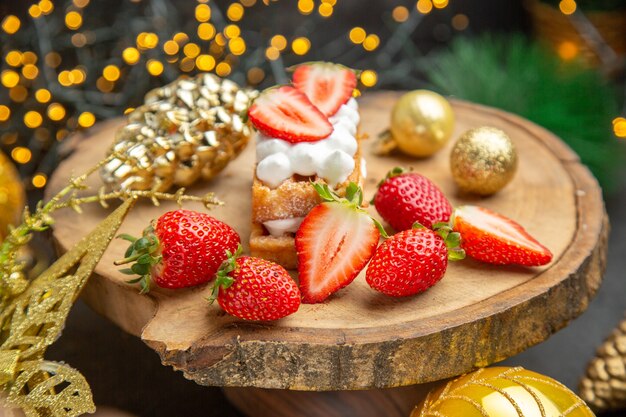 Vista frontal de fresas frescas alrededor de juguetes navideños en el fondo oscuro sabor a fruta foto navideña oscura