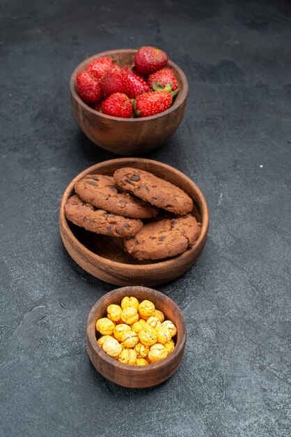 Vista frontal de fresas frescas con galletas sobre fondo oscuro