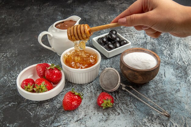 Vista frontal de fresas frescas con miel en la superficie oscura de alimentos dulces de gelatina de frutas