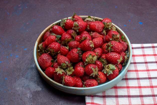 Vista frontal de fresas rojas frescas bayas suaves dentro de un tazón redondo sobre la superficie oscura baya de fruta fresca madura