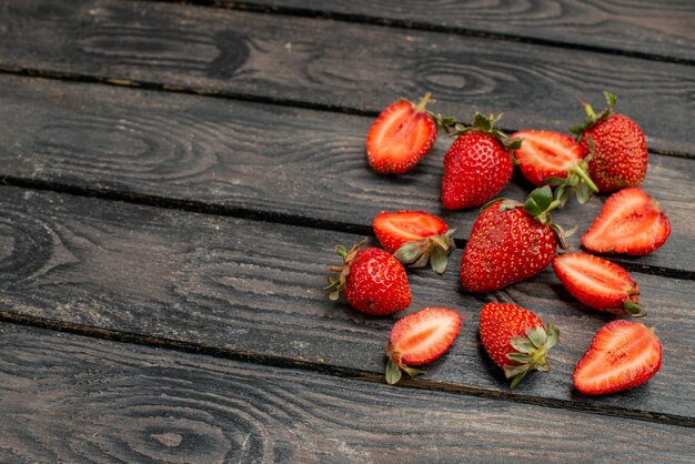 Vista frontal de fresas rojas frescas en rodajas y frutas enteras en un escritorio rústico de madera oscura de color verano jugo de árbol salvaje berry