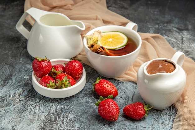 Vista frontal de fresas rojas frescas con una taza de té en la superficie oscura de la baya de frutos rojos