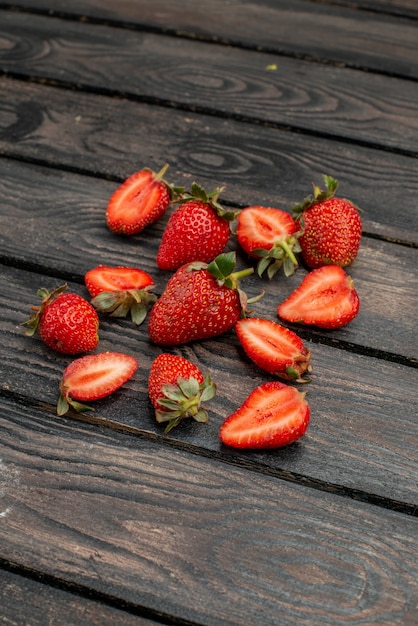 Vista frontal de fresas rojas en rodajas y frutas enteras en el escritorio rústico de madera oscura de color verano jugo de árbol salvaje berry