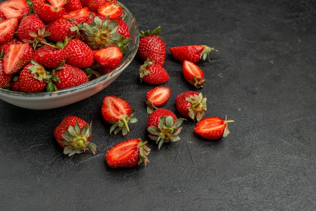 Vista frontal de fresas rojas en rodajas y frutas enteras sobre fondo gris color de verano jugo de árbol salvaje baya