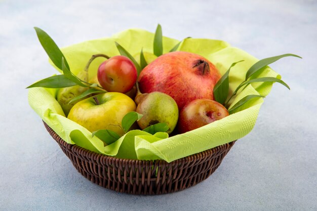 Foto gratuita vista frontal de frutas como ciruela manzana durazno y granada en canasta sobre superficie blanca