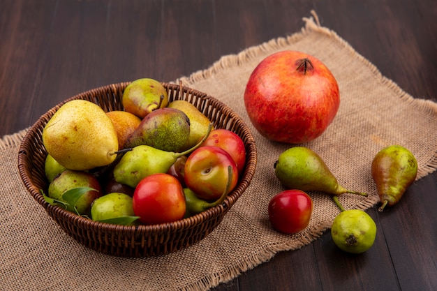 Foto gratuita vista frontal de frutas como durazno manzana ciruela en canasta con granada sobre tela de saco sobre superficie de madera