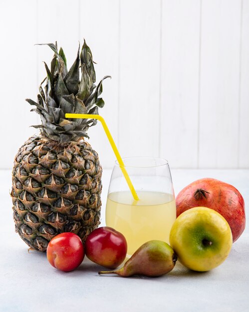 Vista frontal de frutas como piña ciruela manzana durazno y granada con jugo de piña en superficie blanca