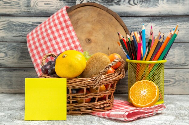 Vista frontal de frutas frescas con pegatina y lápices sobre un fondo gris color de cuaderno de frutas cítricas