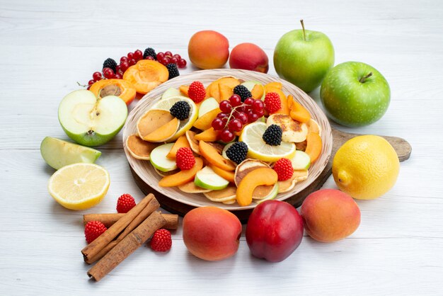 Una vista frontal de frutas frescas en rodajas coloridas y suaves con canelas en el escritorio de madera y alimentos de color de frutas de fondo blanco