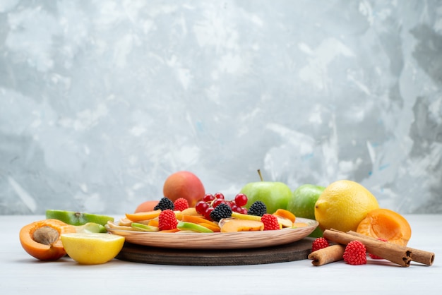 Una vista frontal de frutas frescas en rodajas, suaves y vitamínicas ricas en canela y frutas enteras en el escritorio de madera y fondo blanco.