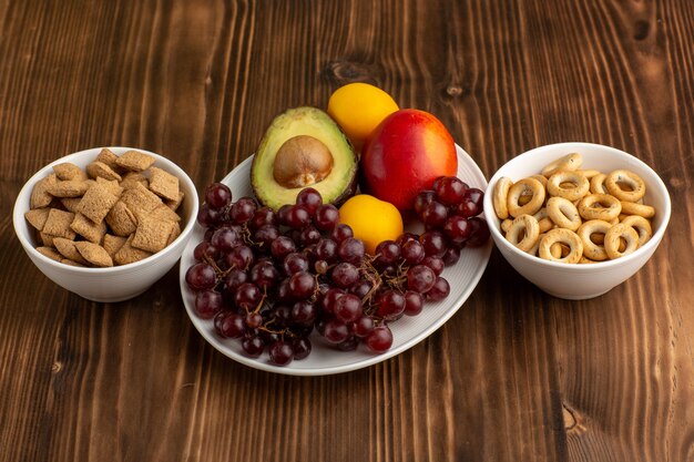 Vista frontal frutas frescas uvas mango aguacate y pomelo con galletas en el escritorio marrón