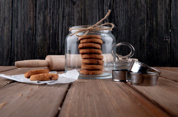 Vista frontal de galletas de avena en un frasco con un rodillo sobre la mesa