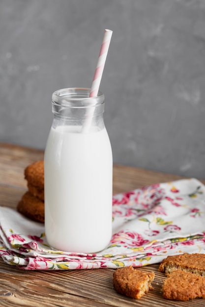 Vista frontal de galletas con botella de leche y paja sobre papel de cocina