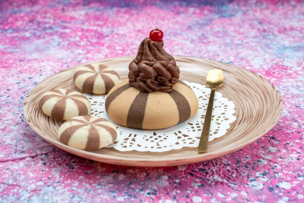 Vista frontal de galletas de chocolate con crema dentro de la placa en la superficie coloreada