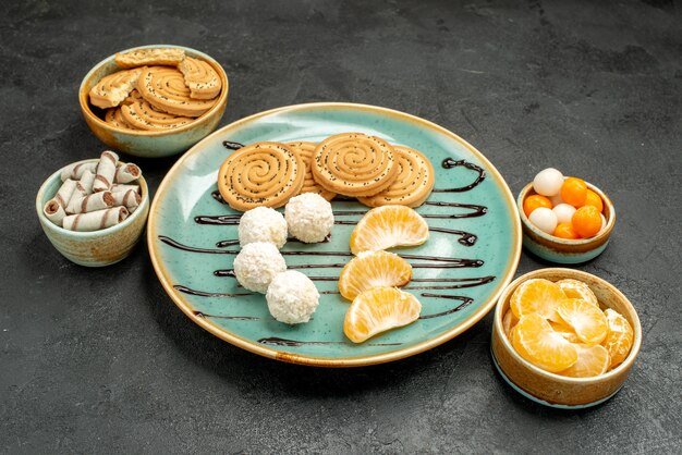 Vista frontal de galletas dulces con caramelos de coco y frutas en caramelo de pastel de galletas de escritorio gris