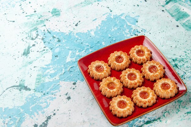 Vista frontal de galletas dulces con mermelada de naranja dentro de la placa roja sobre la superficie azul