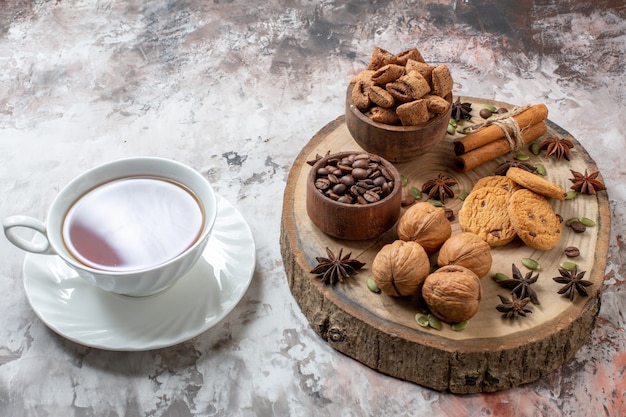 Vista frontal de galletas dulces con taza de té y nueces sobre fondo claro pastel de cacao dulce de galletas de color de té de azúcar