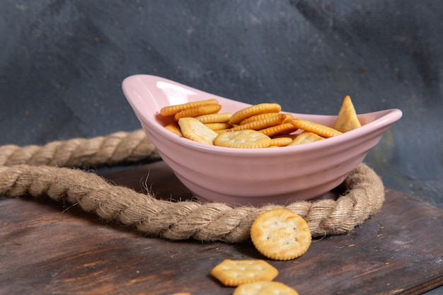 Vista frontal de galletas y galletas dentro de la placa rosa con cuerdas en el escritorio de madera