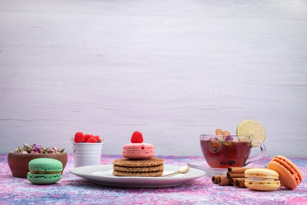 Vista frontal de galletas y macarons con té y canela en el escritorio de luz