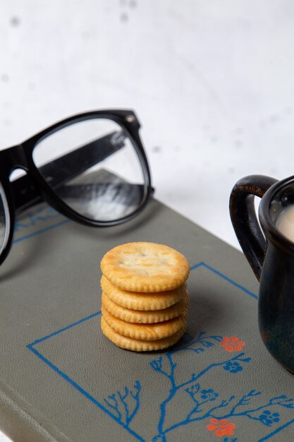 Vista frontal de las galletas redondas con gafas de sol y una taza de leche en un snack crujiente de galleta blanca