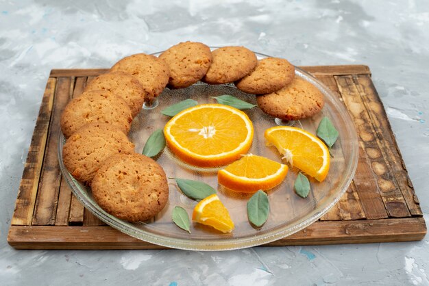 Una vista frontal de las galletas con sabor a naranja con rodajas de naranja fresca dentro de la placa en el escritorio de madera cookie biscuit