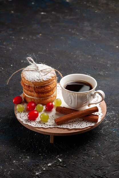 Vista frontal de las galletas sándwich con relleno de crema junto con canela y café en la superficie oscura.