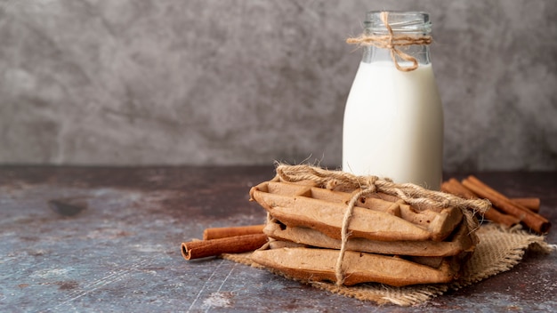 Foto gratuita vista frontal de gofres con palitos de canela y botella de leche