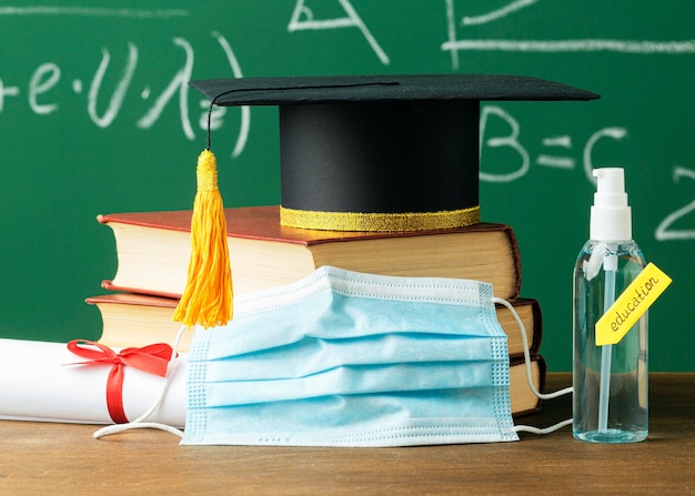 Foto gratuita vista frontal de la gorra académica en libros con máscara médica y desinfectante de manos