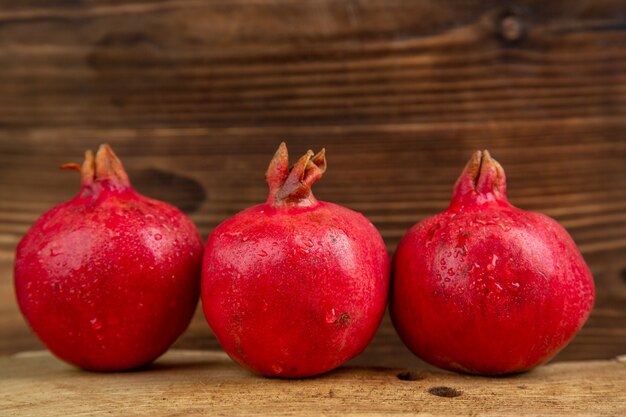 Vista frontal de las granadas frescas en el escritorio de madera de color rojo del árbol de la foto del jugo de fruta