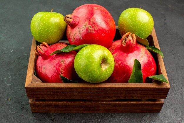 Vista frontal de granadas rojas frescas con manzanas verdes sobre la superficie oscura de color de fruta madura