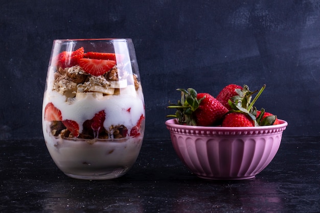 Vista frontal de granola con frutas y nueces en un vaso con fresas en un tazón rosa