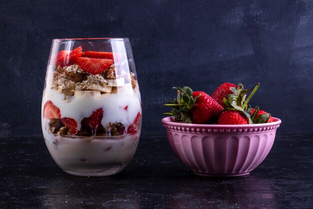 Vista frontal de granola con frutas y nueces en un vaso con fresas en un tazón rosa