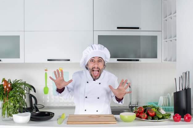 Vista frontal gritando chef masculino en uniforme abriendo las manos detrás de la mesa de la cocina