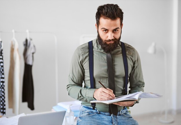 Vista frontal del guapo diseñador de moda masculino en atelier con papeles