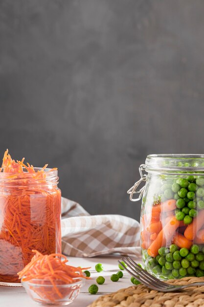 Vista frontal de guisantes en escabeche y zanahorias pequeñas en frascos transparentes con espacio de copia