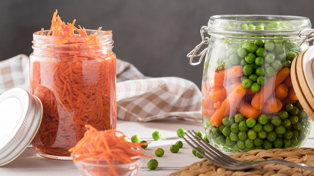 Vista frontal de guisantes en escabeche y zanahorias pequeñas en frascos transparentes