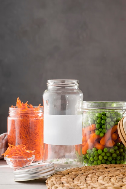 Vista frontal de guisantes en escabeche y zanahorias pequeñas en frascos de vidrio transparente con espacio de copia