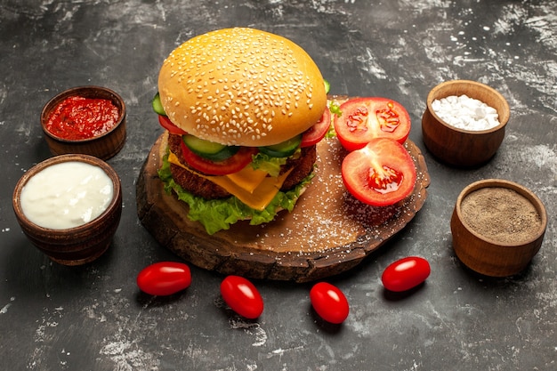 Foto gratuita vista frontal hamburguesa de carne con queso con condimentos en papas fritas de carne de sándwich de pan de superficie oscura